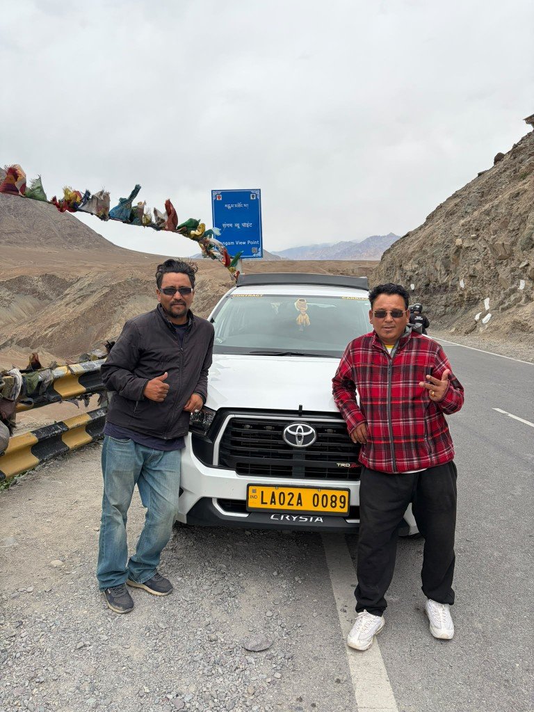 Tashi and Tengeleck with their white Toyota Innova on a high mountain road, prayer flags strung overhead